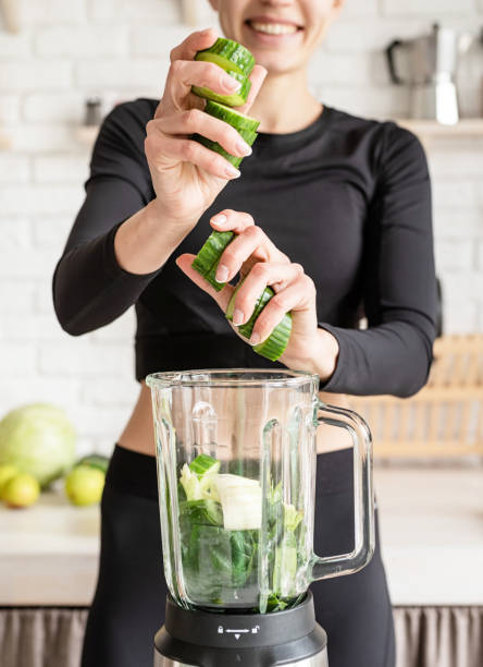 joven mujer rubia sonriente haciendo batido de pepino en la cocina de casa - food processor fotografías e imágenes de stock