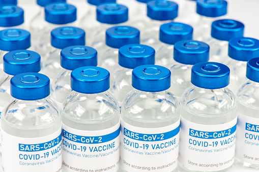 Closeup of a long row of vials with COVID-19 (coronavirus) vaccine. Medical pharmaceutical industry and wholesale (drug distribution) concept.\n\nPlease note: the label of the vial (bottle) was designed and printed by my own, there are no copyright issues. All numbers, names and other information is not real.