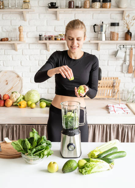 istock Young blond smiling woman making celery smoothie at home kitchen 1291365352