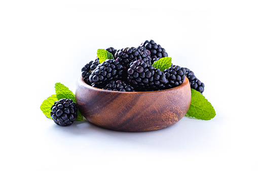 Front view of a wooden bowl full of blackberries with some mint leaves isolated on white background. Studio shot taken with Canon EOS 6D Mark II and Canon EF 100 mm f/ 2.8