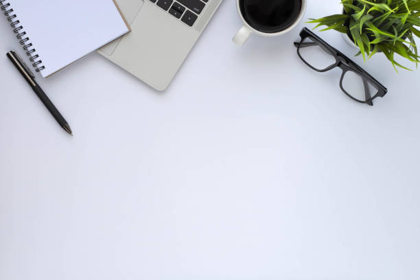 istock Workplace in office with white desk. Top view above of keyboard computer with coffee cup and glasses. Space for modern creative work of designer. Flat lay with copy space. Business-finance concept. 1291371436