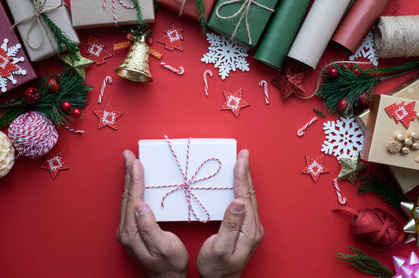 istock Hand with white gift box, christmas holiday on red background. Composition with fir pine branches, ribbon, bow and gift box decorations. Winter, Christmas, new year concept. Flat lay, copy space. 1291371463