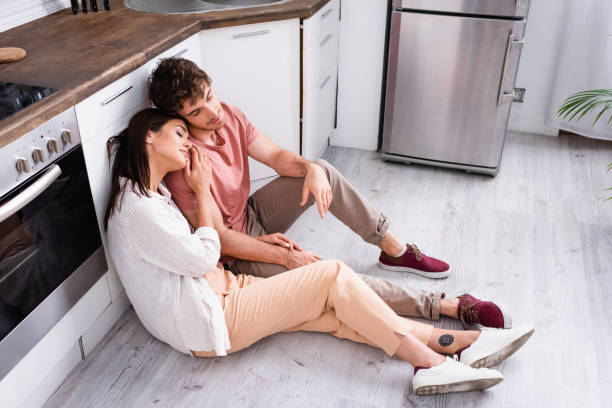 istock Young couple with closed eyes sitting on floor in kitchen 1291376622