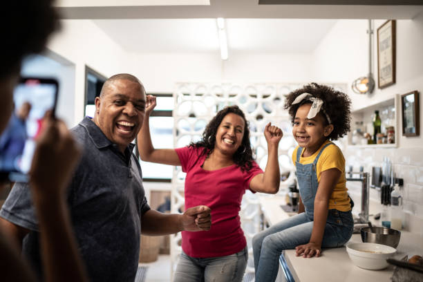 Family dancing in the kitchen while daughter filming them at home Family dancing in the kitchen while daughter filming them at home family reunion celebration stock pictures, royalty-free photos & images