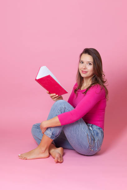 분홍색 배경에 고립 된 그녀의 손에 책을 읽고 바닥에 앉아 그녀의 손에 책을 읽고 미소 유럽 젊은 여성의 초상화 - employee barracks 뉴스 사진 이미지