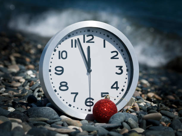 Round clock and red Christmas ball on the beach at midnight