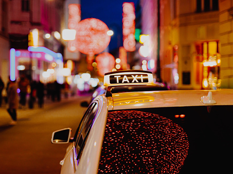 Taxi car during night in the city of Vienna, Austria. Illuminated neon lights in the streets of the town.