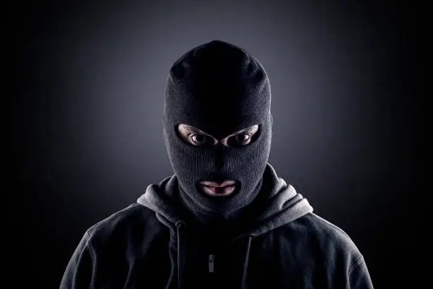 Photo of Criminal wearing black balaclava and hoodie in the dark