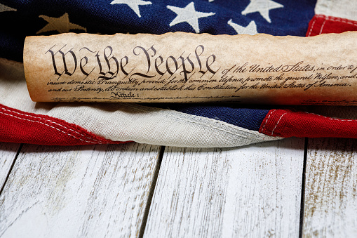 Rolled up copy of the US Constitution with a vintage American flag on white painted weathered wood