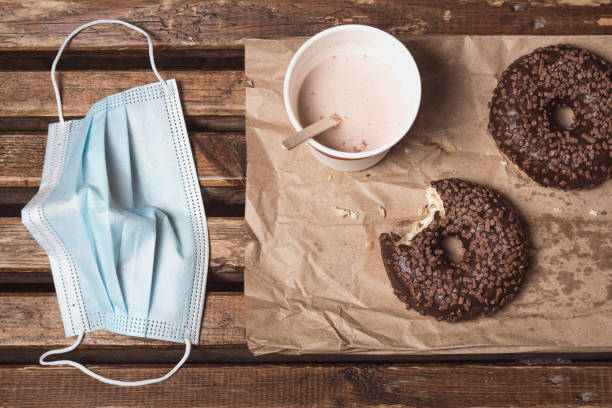 chocolate donuts, milked cocoa in a disposable cup beside a protective mask - 5600 imagens e fotografias de stock