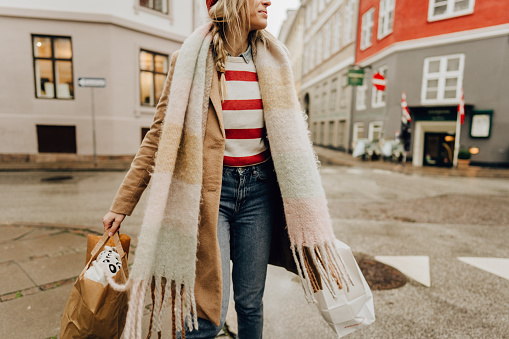 Photo of a young woman carrying paper bags while walking down the street; spending her day outdoors and shopping.