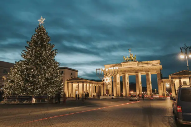 Photo of illuminated menorah symbol and christmas tree in front of Brandenburg gate in Berlin against blue hour sky