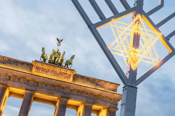 Photo of illuminated menorah symbol in front of Brandenburg gate in Berlin against blue hour sky