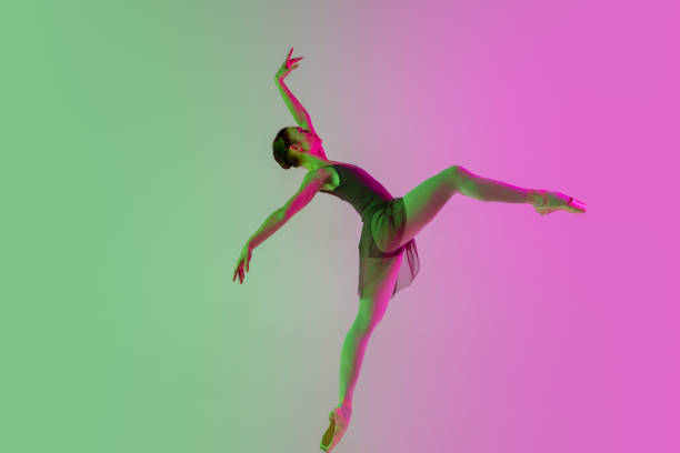 istock Young and graceful ballet dancer isolated on gradient pink-green studio background in neon light. Art in motion 1291412832