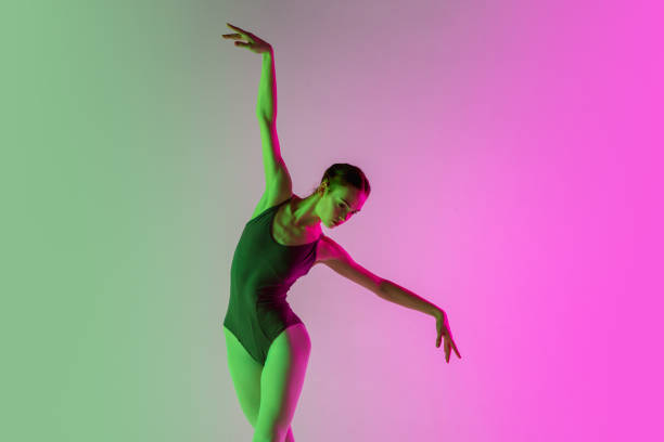 istock Young and graceful ballet dancer isolated on gradient pink-green studio background in neon light. Art in motion 1291412844