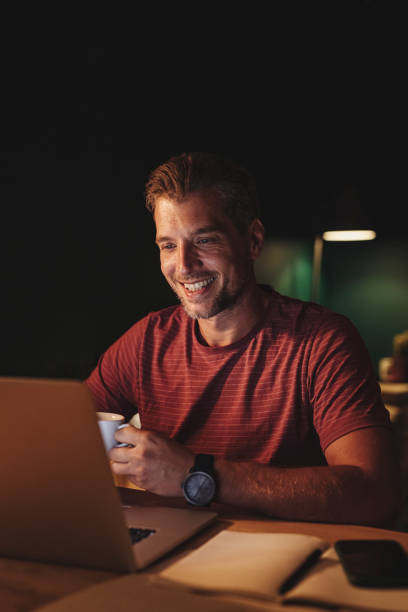 Handsome Happy Young Businessman Holding a Cup of Coffee while while Attending an Online Seminar at Home