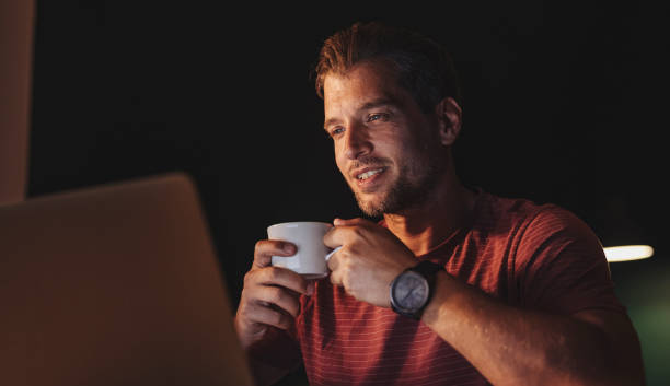 istock Handsome Happy Young Businessman Holding a Cup of Coffee while while Attending an Online Seminar at Home 1291413584