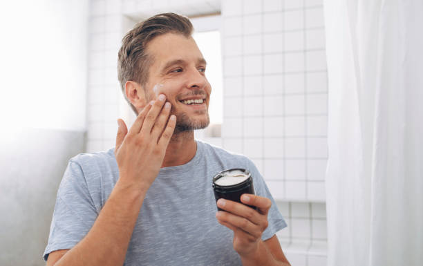 jovem bonito aplicando um moisurizer pós-barba depois de uma barba matinal - pêlo facial - fotografias e filmes do acervo