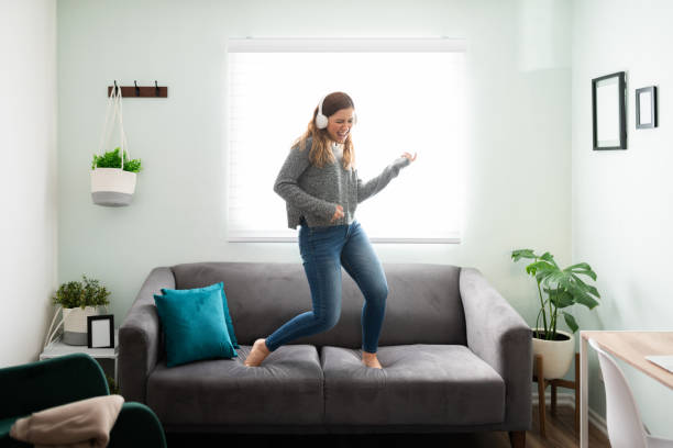 istock Enthusiastic woman singing with headphones on her sofa 1291414318