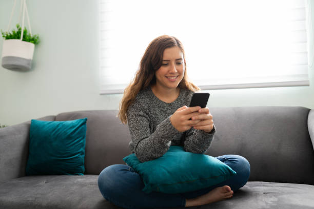 istock Young woman smiling on the sofa while sending a text on her smartphone 1291415352