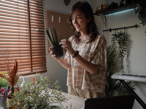 Asian female having happiness while setting up a flower pot on the desk in her room.