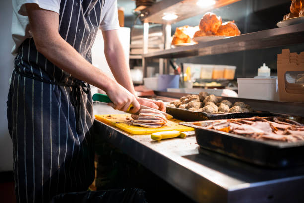 Slicing the Sunday Roast An unrecognisable chef working in a commercial kitchen wearing chefs whites and an apron. He is cutting meat on a chopping board and has various trays of food around him. food hygene stock pictures, royalty-free photos & images