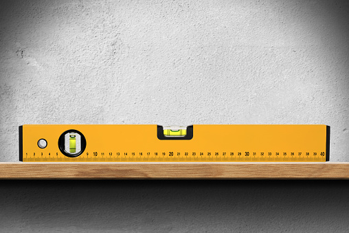 Closeup of an orange bubble level or spirit level on a wooden shelf on white wall.