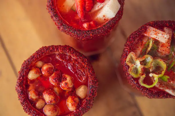 Photo of Michelada beer with tomato juice. Clamato with beer on wooden table. Mexican drink.