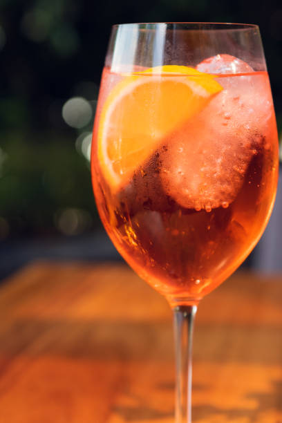 istock Orange cocktail with orange garnish in wine glass, Spritz in sunny setting. 1291421826