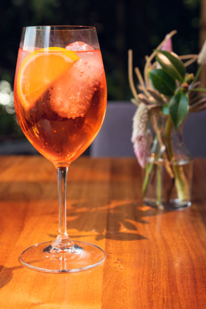 istock Orange cocktail with orange garnish in wine glass, Spritz in sunny setting. 1291422488