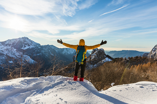 Hiker on snowy mountain with hands raised to the clear sky