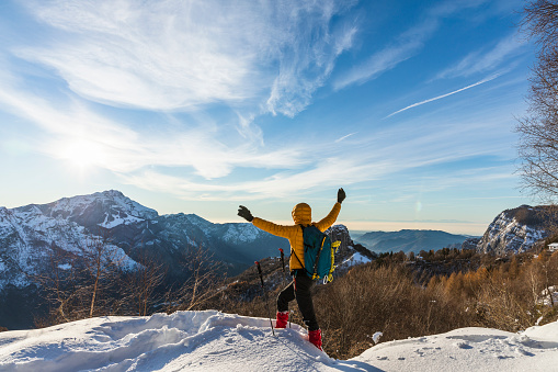 Hiker on snowy mountain with hands raised to the clear sky