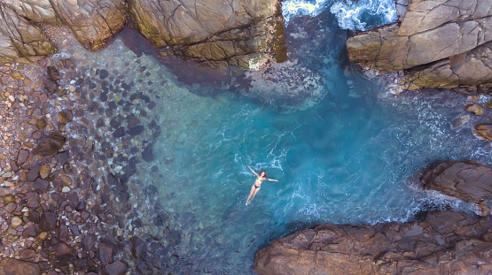 Aerial view of young woman in the blue sea among rocks, oaxaca mexico from above.