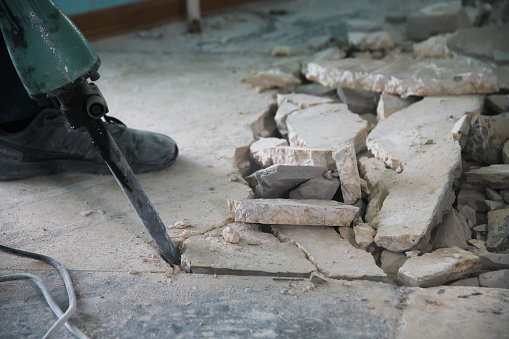 A worker uses a jackhammer to remove a layer of old cement screed inside the repaired room. Construction