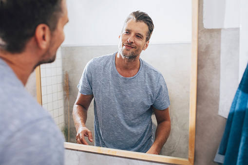 Handsome young Caucasian man checking out his beard in a bathroom mirror after a morning shave at home.