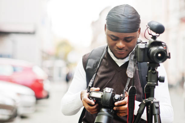 Professional african videographer Young professional african american videographer holding professional camera with tripod pro equipment. Afro cameraman wearing black duraq making a videos. do rag stock pictures, royalty-free photos & images