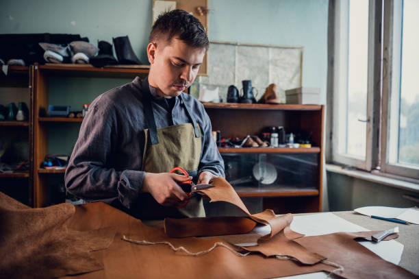 istock In a boot shop, an experienced young master cuts out leather shoe elements with scissors 1291440447
