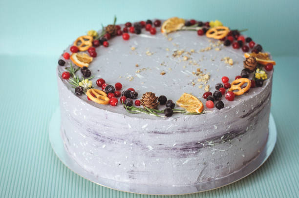 istock gently violet creamy cake decorated with blueberries, cranberries, oranges, cones. Gray round cake on a blue background, decorated in New Year's style. 1291441890