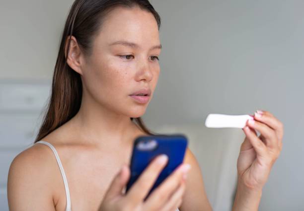 A woman waiting for pregnancy test results, holding her phone. A serious woman watching her test looking a hoping its positive, trying to get pregnant. ovulation stock pictures, royalty-free photos & images