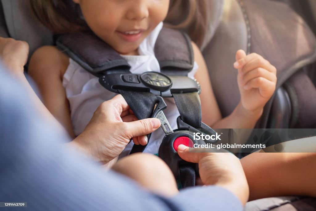 Parent buckling her child's seat belt in the car. Transportation safety. A toddler sitting in the child car seat with the mother helping to buckle and fasten seat beat properly to stay safe while driving. Car Safety Seat Stock Photo
