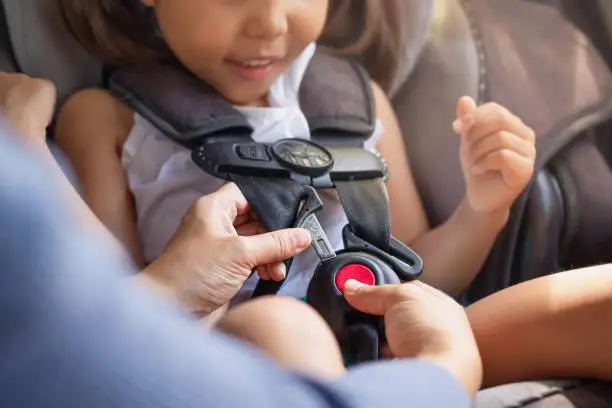 Photo of Parent buckling her child's seat belt in the car. Transportation safety.