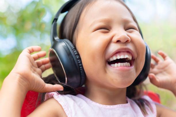 menina feliz ouvindo música em seus telefones da cabeça, sorrindo de alegria ao ar livre. - preschooler child chinese ethnicity asian ethnicity - fotografias e filmes do acervo