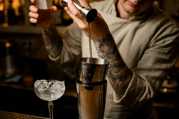istock Man bartender pours drink from metal jigger into shaker on bar counter 1291450091