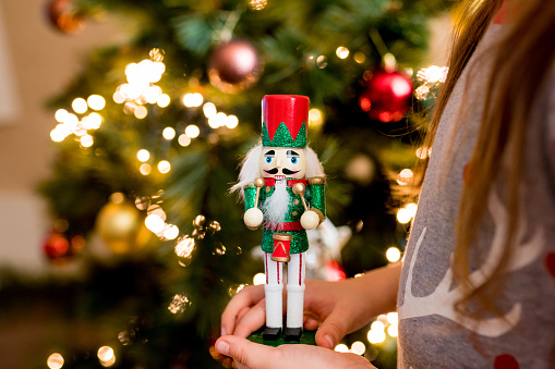 Close-up of child girl holding wooden nutcracker toy in hands. Christmas decoration symbol.