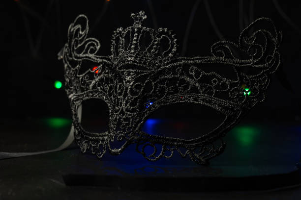 istock Black festive carnival mask on a black background with multi-colored garlands. 1291460339