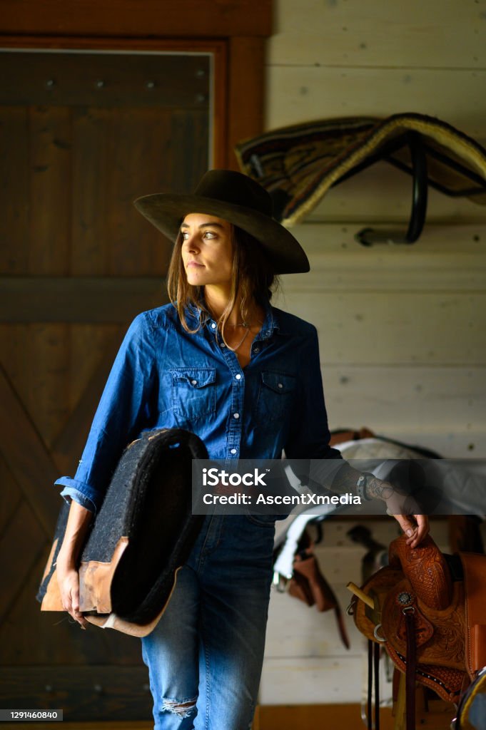 Female rancher in a tacking room Female farmer in a tacking room. Rancher working on a Canadian ranch. Empowered woman working in agriculture. Cowgirl Stock Photo