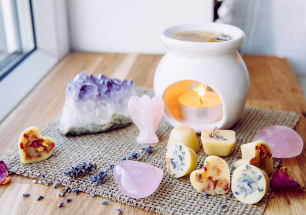 Homemade mini wax melts in aromatherapy lamp diffuser at home interior with rose quartz crystal hearts and angel for decoration on wooden window sill on winter. Seasonal spiritual zen concept. Homemade mini wax melts in aromatherapy lamp diffuser at home interior with rose quartz crystal hearts and angel for decoration on wooden window sill on winter. Seasonal spiritual zen concept. candle wax stock pictures, royalty-free photos & images