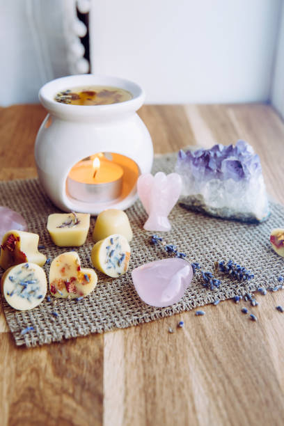Homemade mini wax melts in aromatherapy lamp diffuser at home interior with rose quartz crystal hearts and angel for decoration on wooden window sill on winter. Seasonal spiritual zen concept.