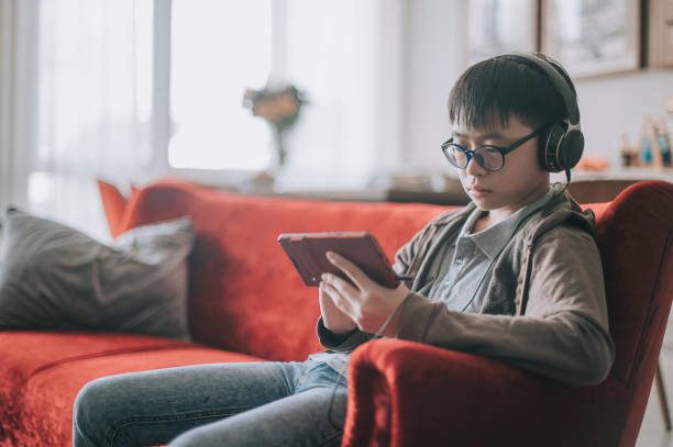 aziatische chinese tiener die mobiel spel met hoofdtelefoon op bank in woonkamer speelt - alleen één tienerjongen stockfoto's en -beelden