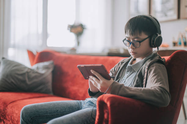 Asian chinese teenage boy playing mobile game with headphone on sofa in living room Asian chinese teenage boy playing mobile game with headphone on sofa in living room one teenage boy only stock pictures, royalty-free photos & images